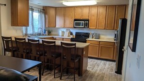 Una cocina con armarios de madera, microondas, estufa y comedor con sillas y una mesa.