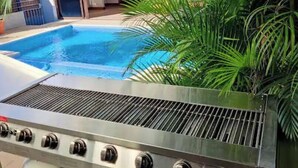 Una piscina amb una barbacoa i plantes en test properes.