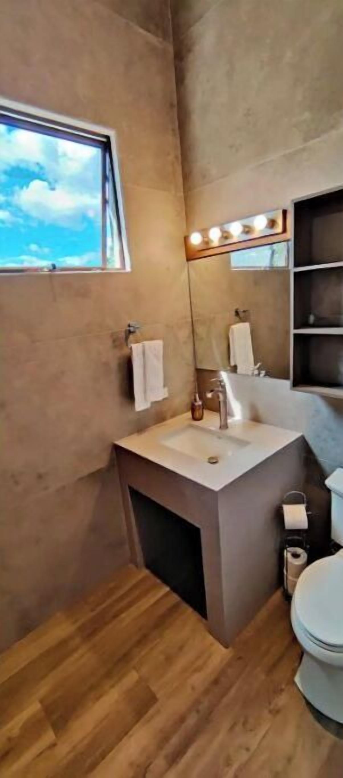 Une salle de bain moderne dotée d’une grande fenêtre, d’un meuble-lavabo avec un miroir et de toilettes.