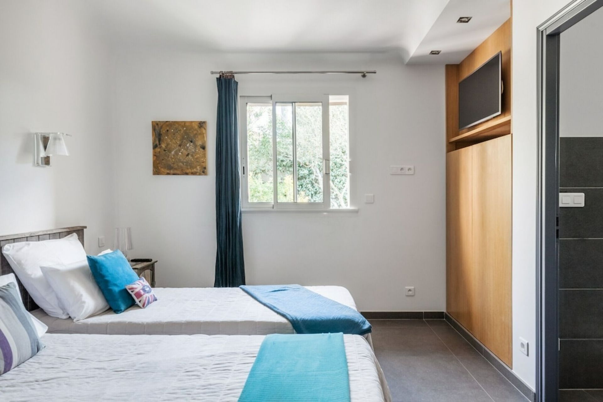 Ein Schlafzimmer mit zwei Betten, einem fensterbelaubten Fenster, einem Bild an der Wand und einem Kleiderschrank.