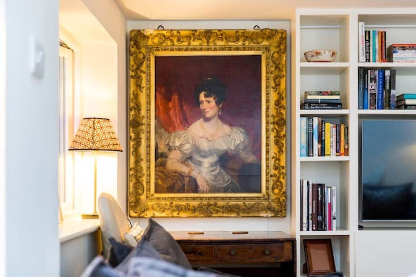 Quarto com um retrato grande emoldurado, uma estante de livros e uma luminária.