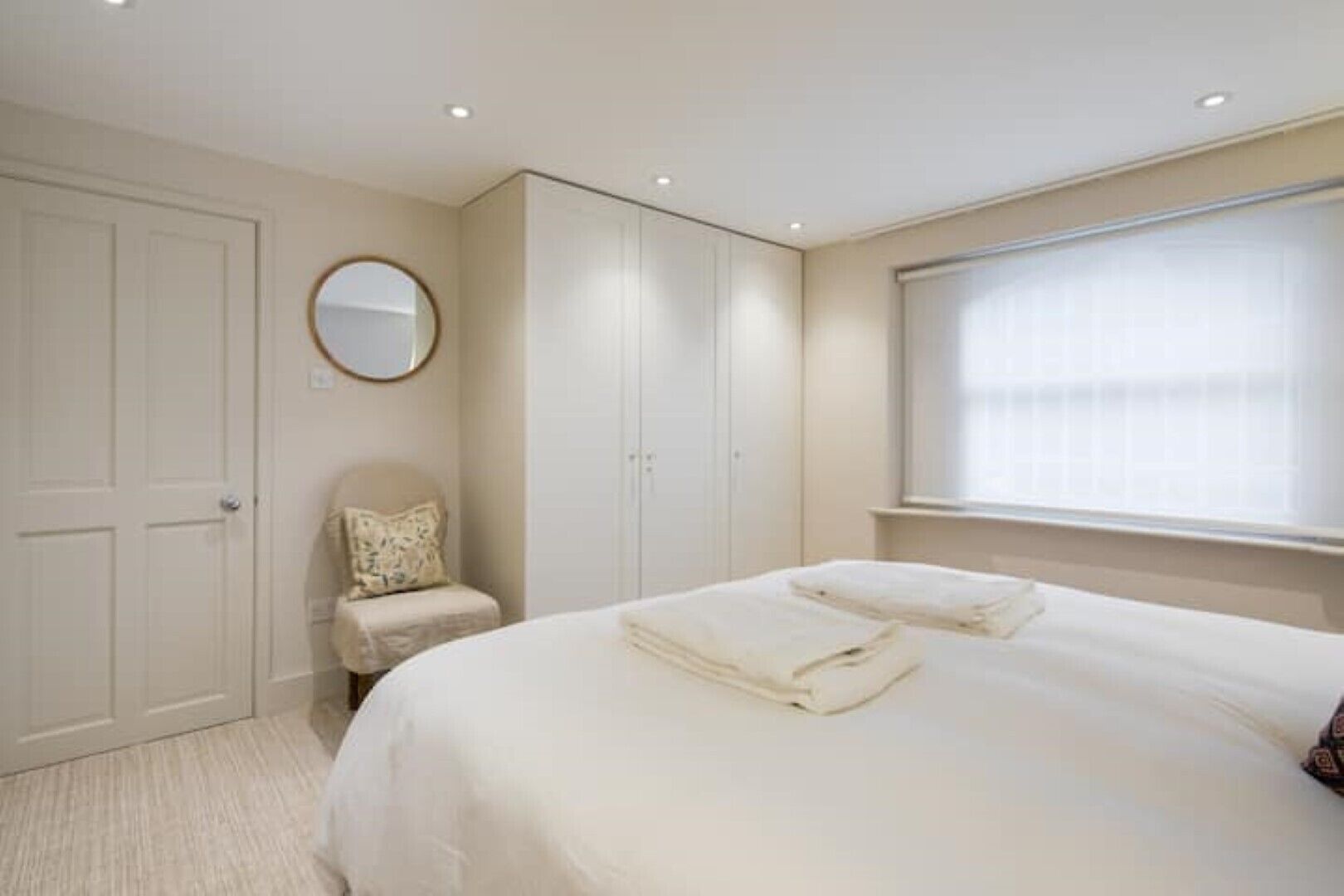 A bedroom with a large bed, a chair, a wardrobe, and a window with blinds.