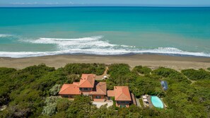 A coastal property with a swimming pool, surrounded by lush greenery and a view of the ocean.