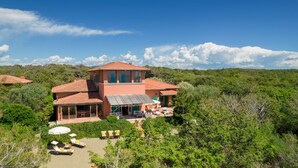 A large, two-story house with a red-tiled roof, surrounded by lush greenery and a clear blue sky. - Villa Corallina 12, Emma Villas (Marina di Bibbona)