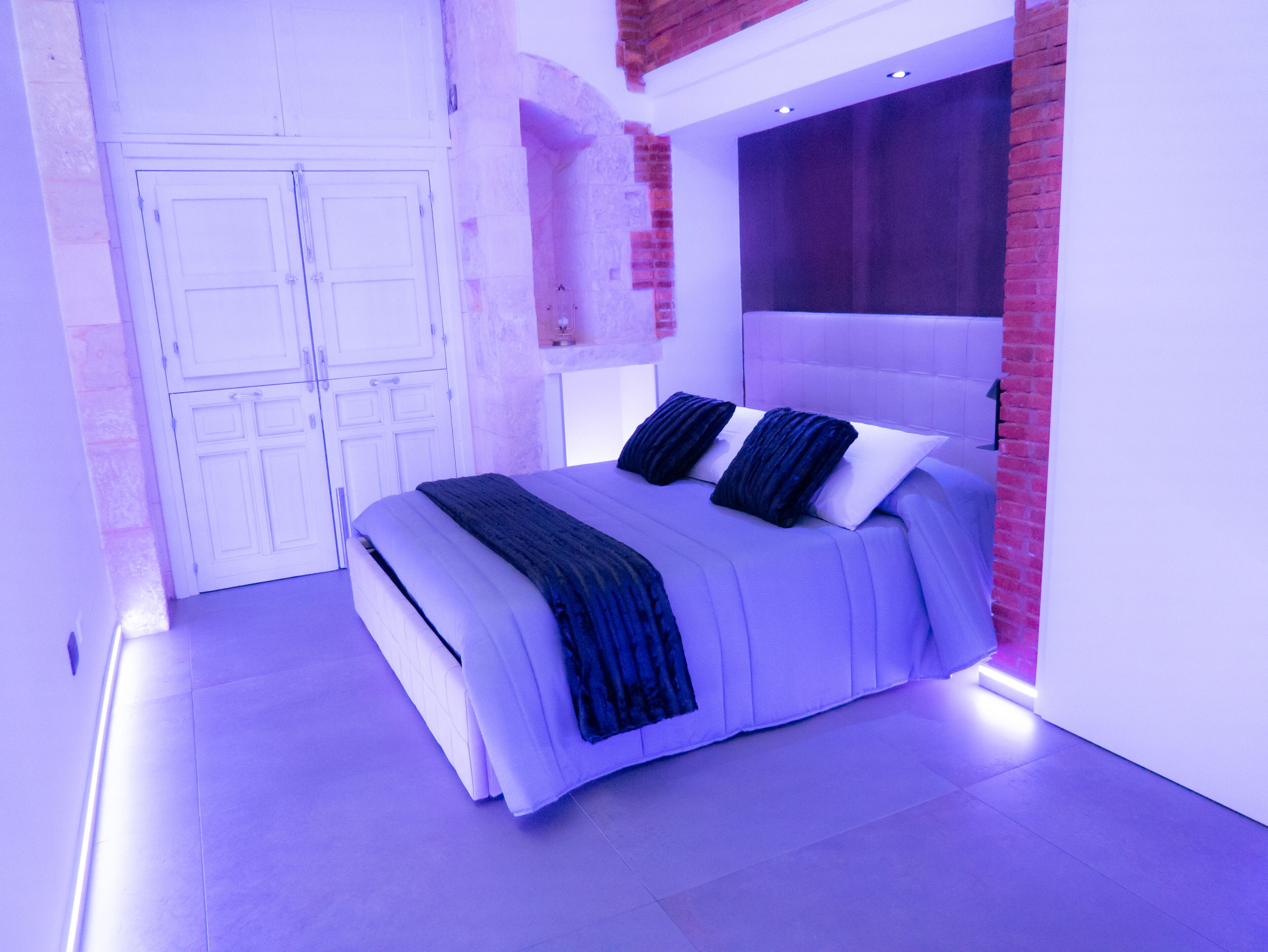 A modern bedroom with a large bed, white walls, and a brick accent wall.