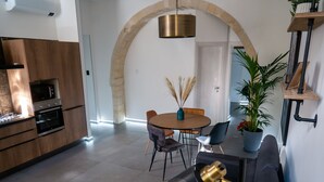 A modern kitchen with built-in appliances, a dining area with a round table and chairs, and a cozy seating area with a sofa and a side table. - Elegante Suite a piano terra di un palazzo storico del 1700 - Centro di Ortigia. (Siracusa)