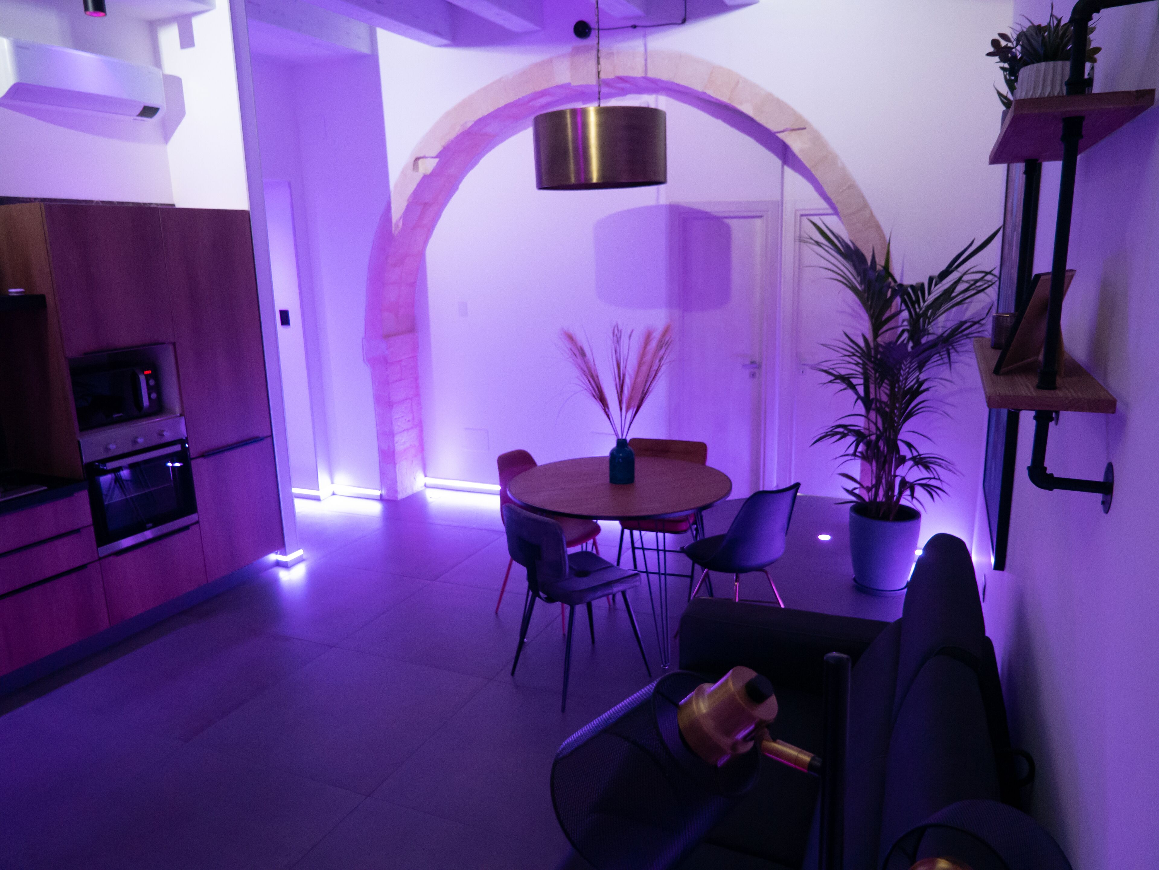 Une cuisine moderne équipée d’un four à micro-ondes, d’un four et d’un lave-vaisselle encastré. On y trouve également un coin repas avec une table ronde et des chaises, ainsi qu’une plante en pot.