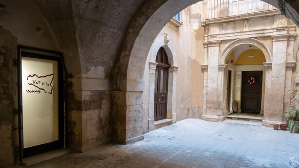 An interior courtyard with stone flooring, arched doorways, and a framed map on a wall. - Elegante Suite a piano terra di un palazzo storico del 1700 - Centro di Ortigia. (Siracusa)