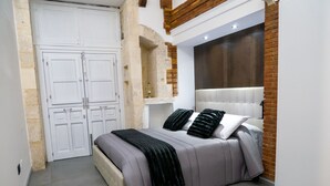 A bedroom with a bed, a wardrobe, and a brick wall. - Elegante Suite a piano terra di un palazzo storico del 1700 - Centro di Ortigia. (Siracusa)