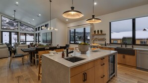 Una cocina moderna con una isla grande, armarios de madera y vistas a un paisaje nevado a través de amplios ventanales.