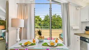 Un coin repas avec une table dressée pour deux personnes, agrémenté d’un saladier rempli de fruits tropicaux, de deux boissons et d’une lampe.