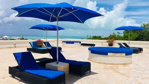 A beachside lounge area with blue umbrellas, lounge chairs, and a pool. - Oasis -1 Studio Condo -Tropical Views -Wifi hot tub & Pool. 10min walk to beach. (TURTLE COVE)