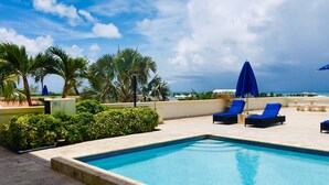 A swimming pool with lounge chairs and umbrellas, surrounded by palm trees and a view of the ocean. - Oasis -1 Studio Condo -Tropical Views -Wifi hot tub & Pool. 10min walk to beach. (TURTLE COVE)