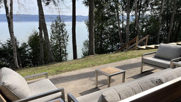 An outdoor seating area with a view of a lake, surrounded by trees. - Big Glen Lake - Beechwood Cottage (Glen Arbor)