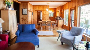 A wooden cabin interior with a dining area, two sofas, and a kitchen. - Big Glen Lake - Beechwood Cottage (Glen Arbor)
