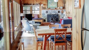 A cozy cabin interior with wooden walls, a dining area with a table and chairs, a kitchen with a stove, and a refrigerator. - Big Glen Lake - Beechwood Cottage (Glen Arbor)