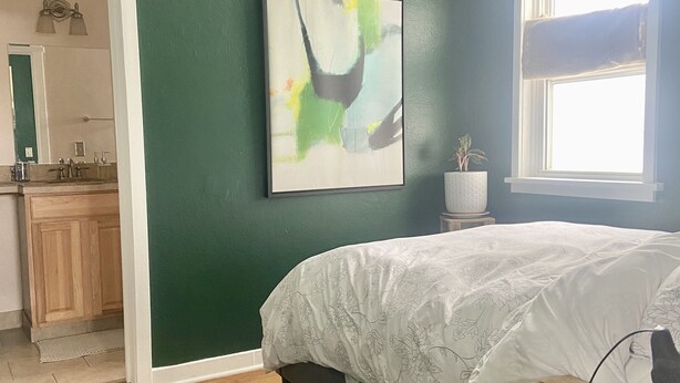 Ein Schlafzimmer mit Bett, grüner Wand, Fenster und einem Bild.