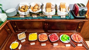 Un bufé con alimentos identificados, incluyendo pan, bollos y diversas frutas y verduras.