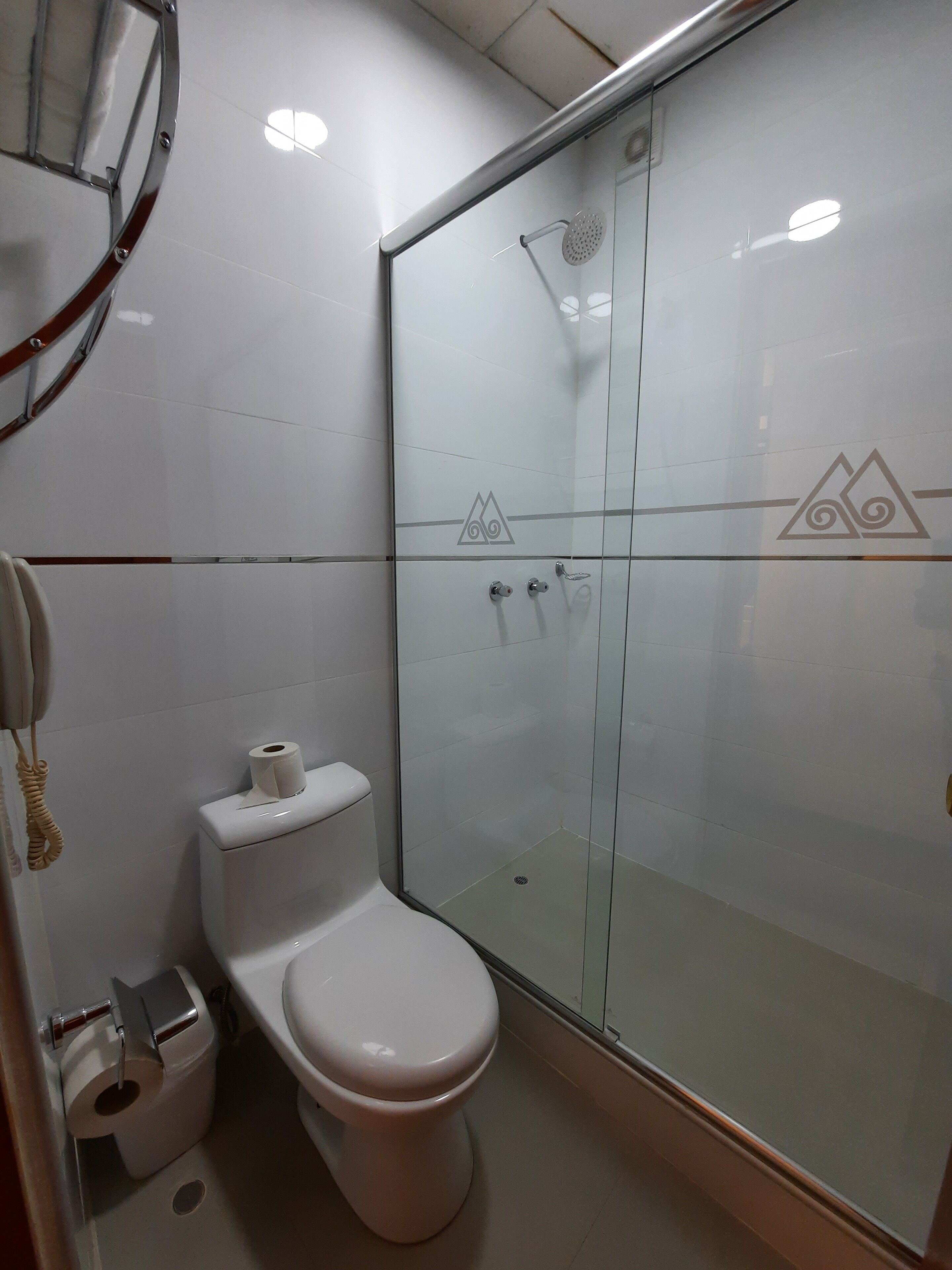 Un baño con inodoro, cabina de ducha de vidrio y dispensador de papel higiénico.