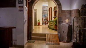 Un pasillo que conduce a una habitación con pared de piedra, puerta de madera y señalización de zona de seguridad.
