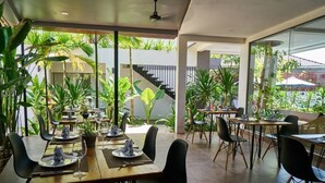 Een restaurant met gedekte tafels, omgeven door grote ramen en binnenshuis planten.