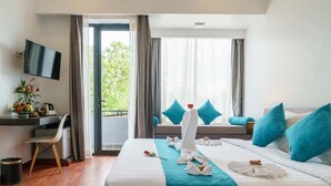 Een hotelkamer met twee bedden, een bureau, een televisie en een balkon met uitzicht op groen.