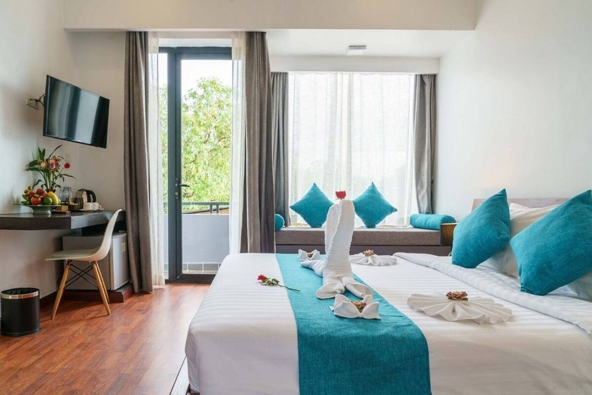 Une chambre d’hôtel avec deux lits, un bureau, une télévision et un balcon donnant sur un espace verdoyant.