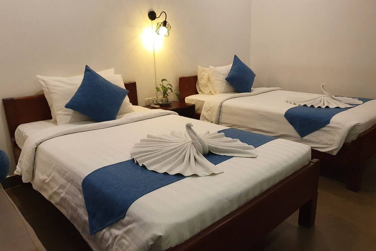 Une chambre d’hôtel avec deux lits, chacun agrémenté de draps blancs et de touches de bleu, une table de chevet avec une lampe et un luminaire fixé au mur.