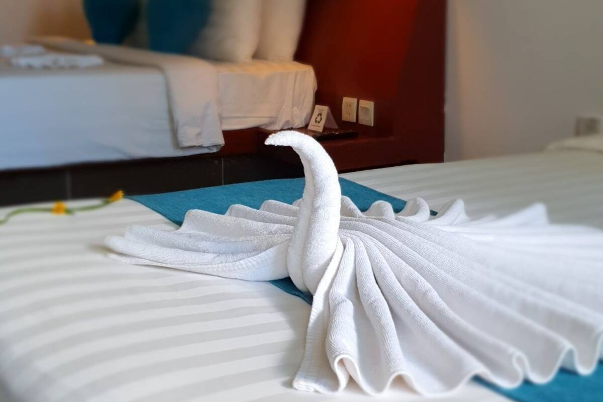 Un lit bien fait, avec une serviette pliée en forme de cygne, une couvre-lit à rayures et une petite décoration florale.