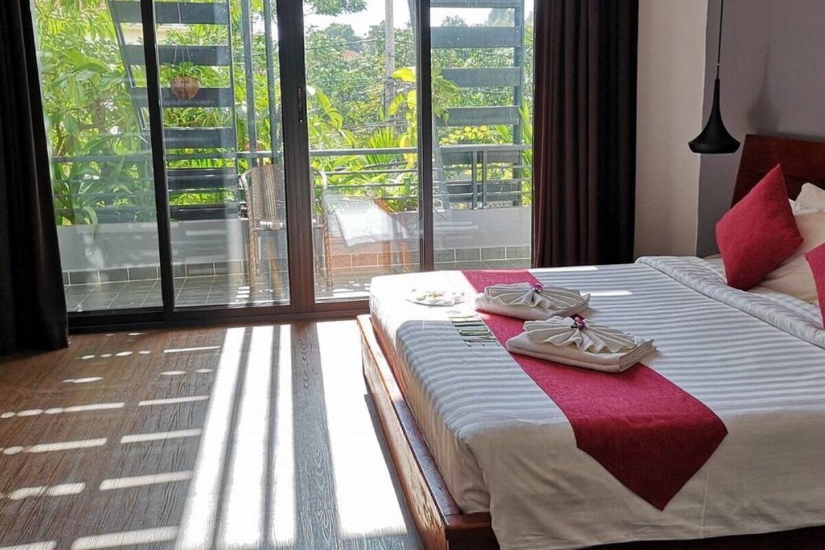 Une chambre d’hôtel avec un lit, un plaid rouge et une vue sur la verdure grâce à de grandes portes coulissantes.