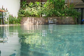 A clear pool with a stone wall and lush greenery in the background. - Siem Reap Tevi Residence (Siem Reap)