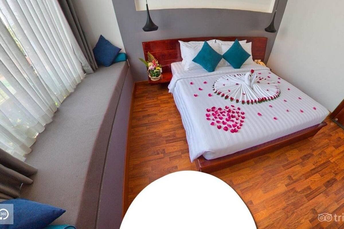 Un lit bien fait, agrémenté de pétales de fleurs décoratives, avec une tête de lit en bois et une table de chevet surmontée d’une lampe.