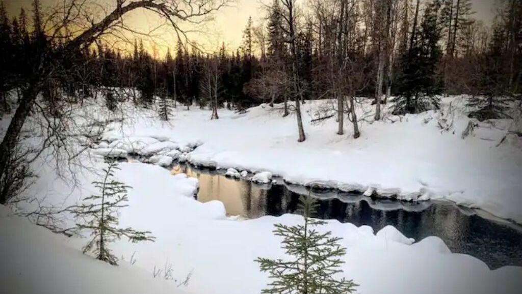 A snowy landscape with a frozen river, trees, and a clear sky.