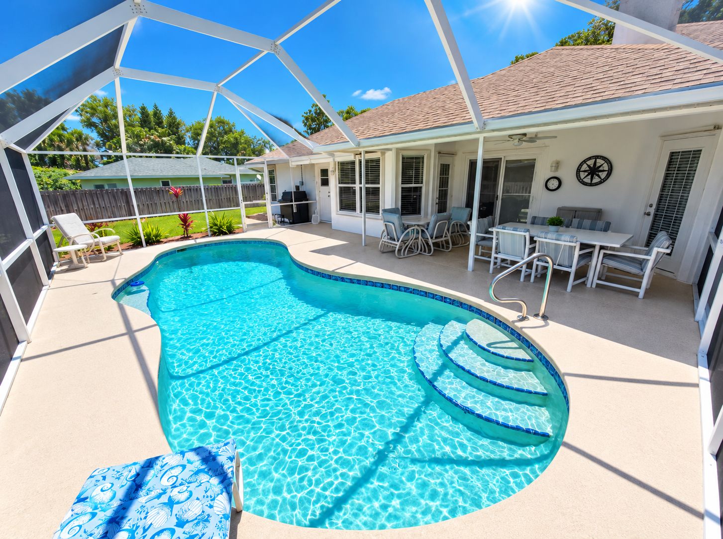 A swimming pool with a covered patio area, outdoor furniture, and a fenced yard.