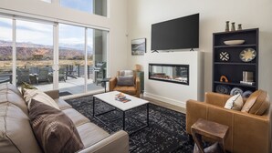 A modern living room with a fireplace, a flat-screen TV, and a balcony with outdoor seating. - Magnificent 4 bedroom New home with views minutes from Arches (Moab)