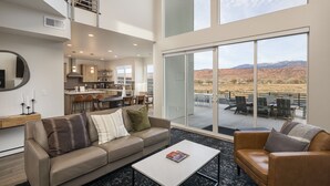 A spacious living area with a large window overlooking a scenic landscape, a modern kitchen, and a cozy seating area. - Magnificent 4 bedroom New home with views minutes from Arches (Moab)