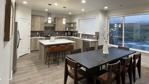 A modern kitchen with a large island, bar stools, and a dining table with chairs. - Magnificent 4 bedroom New home with views minutes from Arches (Moab)