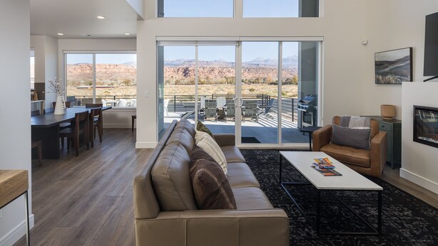A spacious living room with a large sliding glass door leading to a patio with outdoor furniture. - Magnificent 4 bedroom New home with views minutes from Arches (Moab)