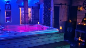 A hot tub with a wooden base, surrounded by ambient lighting and decorative elements like candles and wall-mounted lights. - Escape with Rooftops" with PAID OPTION "JACCUZZI - SAUNA (Fécamp)