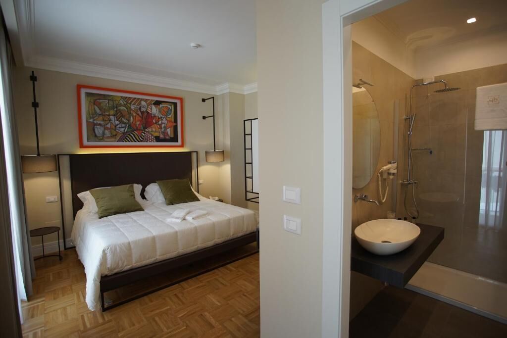 A bedroom with a bed, bedside tables, a painting, and a bathroom with a sink and shower.