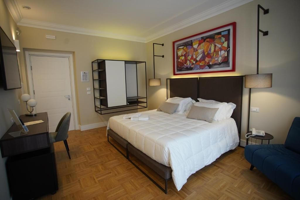 A hotel room with a bed, desk, chair, and a painting on the wall.