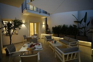 Un comedor al aire libre bien iluminado con una mesa preparada para dos personas, rodeado de asientos cómodos y plantas en macetas.
