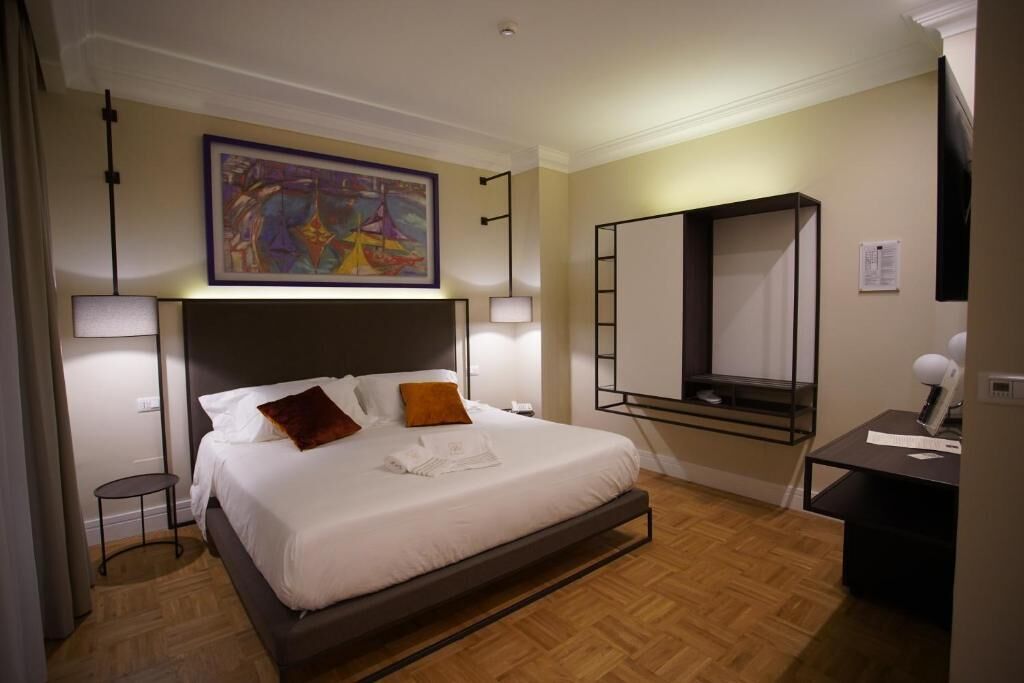 Habitación de hotel ordenada con una cama grande, una mesita de noche, un escritorio y un televisor montado en la pared.