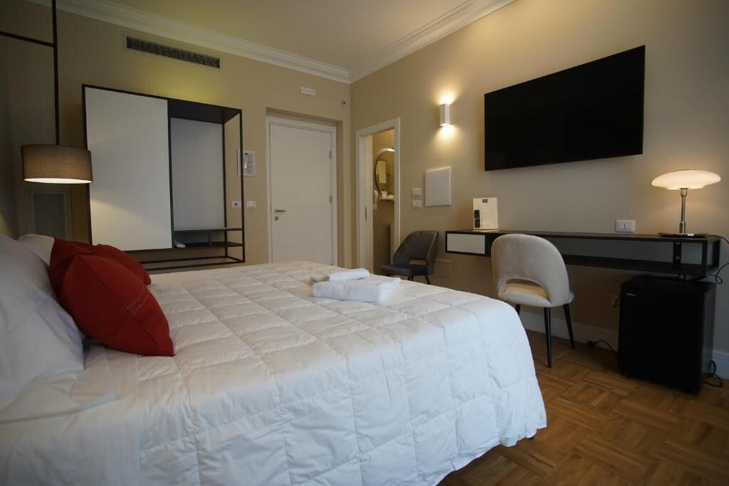 A hotel room with a large bed, a desk, a chair, and a TV mounted on the wall.