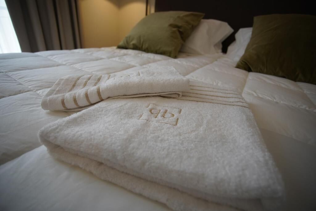 Un lit bien fait, avec une serviette blanche pliée et un oreiller recouvert d’une housse verte.