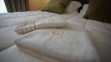 Un lit bien fait, avec une serviette blanche pliée et un oreiller recouvert d’une housse verte.
