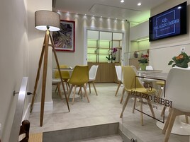 Un comedor moderno con sillas amarillas y blancas, una lámpara de pie y un televisor que muestra