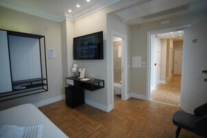Una habitación de hotel moderna con una cama, un televisor montado en la pared, un pequeño escritorio con una lámpara y suelo de madera.
