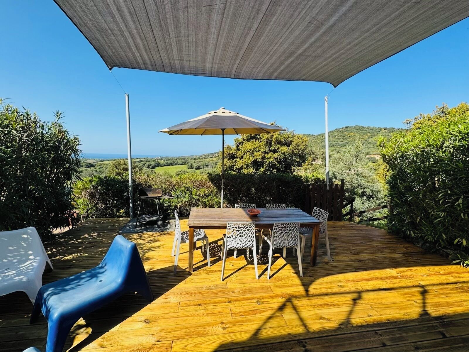 An outdoor patio with a wooden deck, a table with chairs, and a large umbrella providing shade.