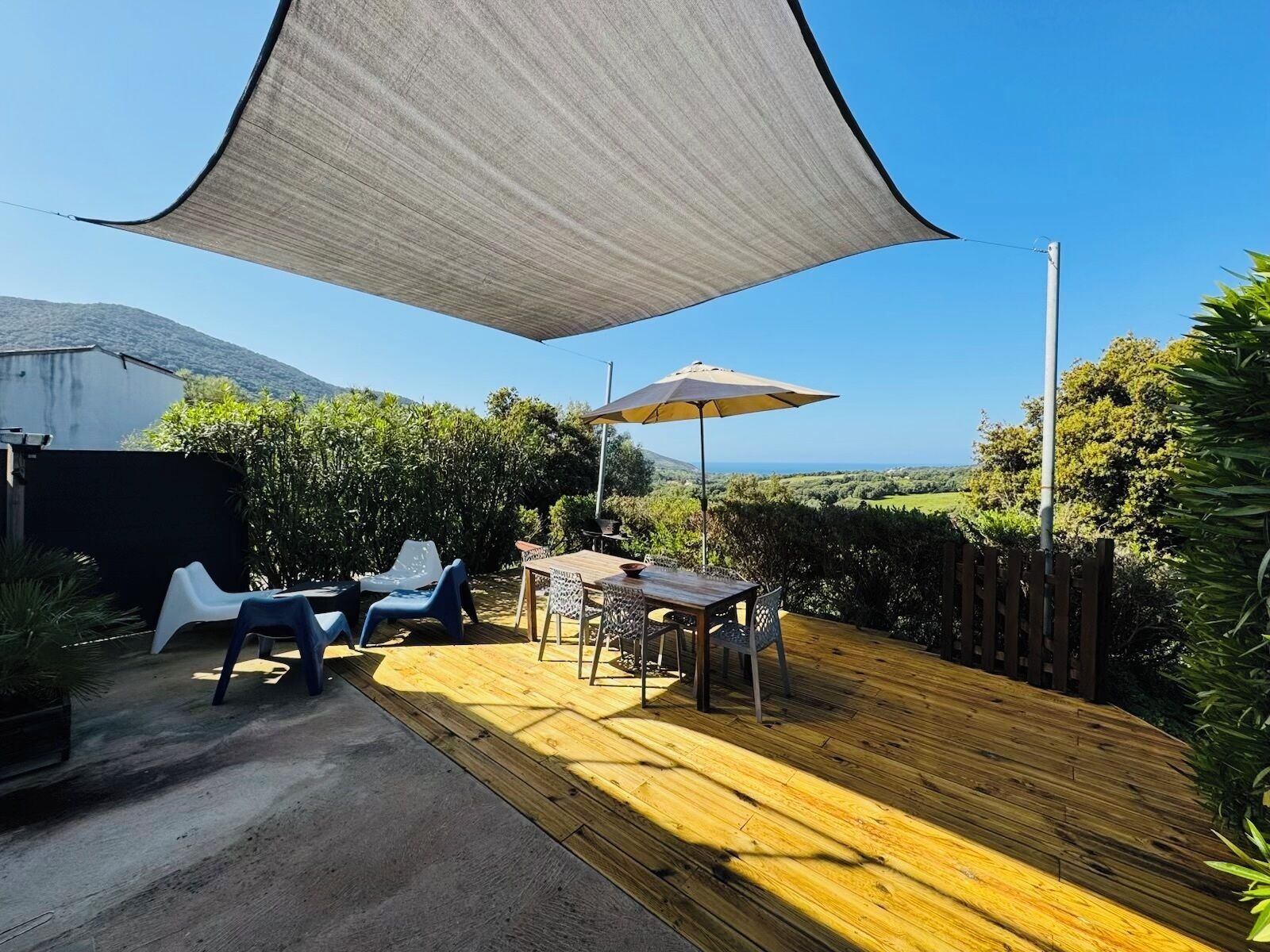 An outdoor patio with a wooden deck, a table with chairs, and a large shade sail.